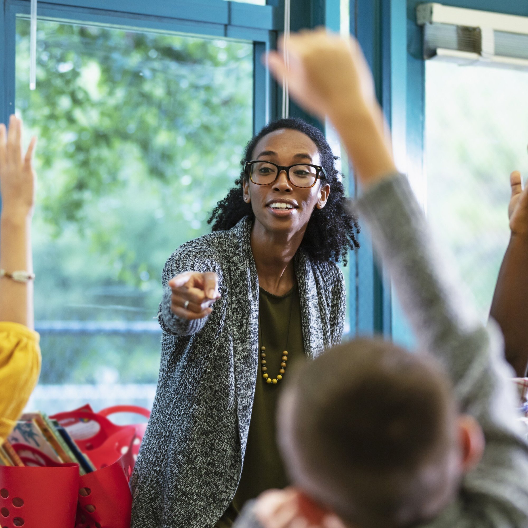 teacher pointing to young students with hands raised