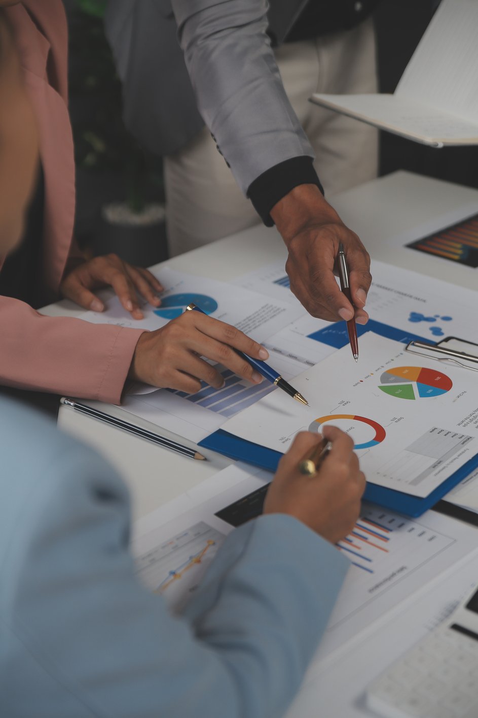 three people pointing at data on pages laid out on a table.