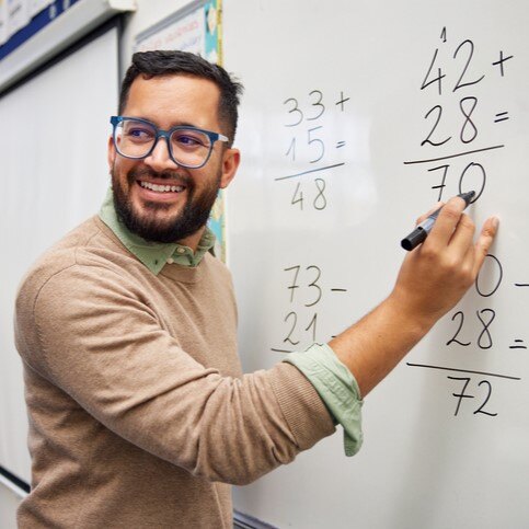 Smiling math teacher pointing to equations drawn on a whiteboard